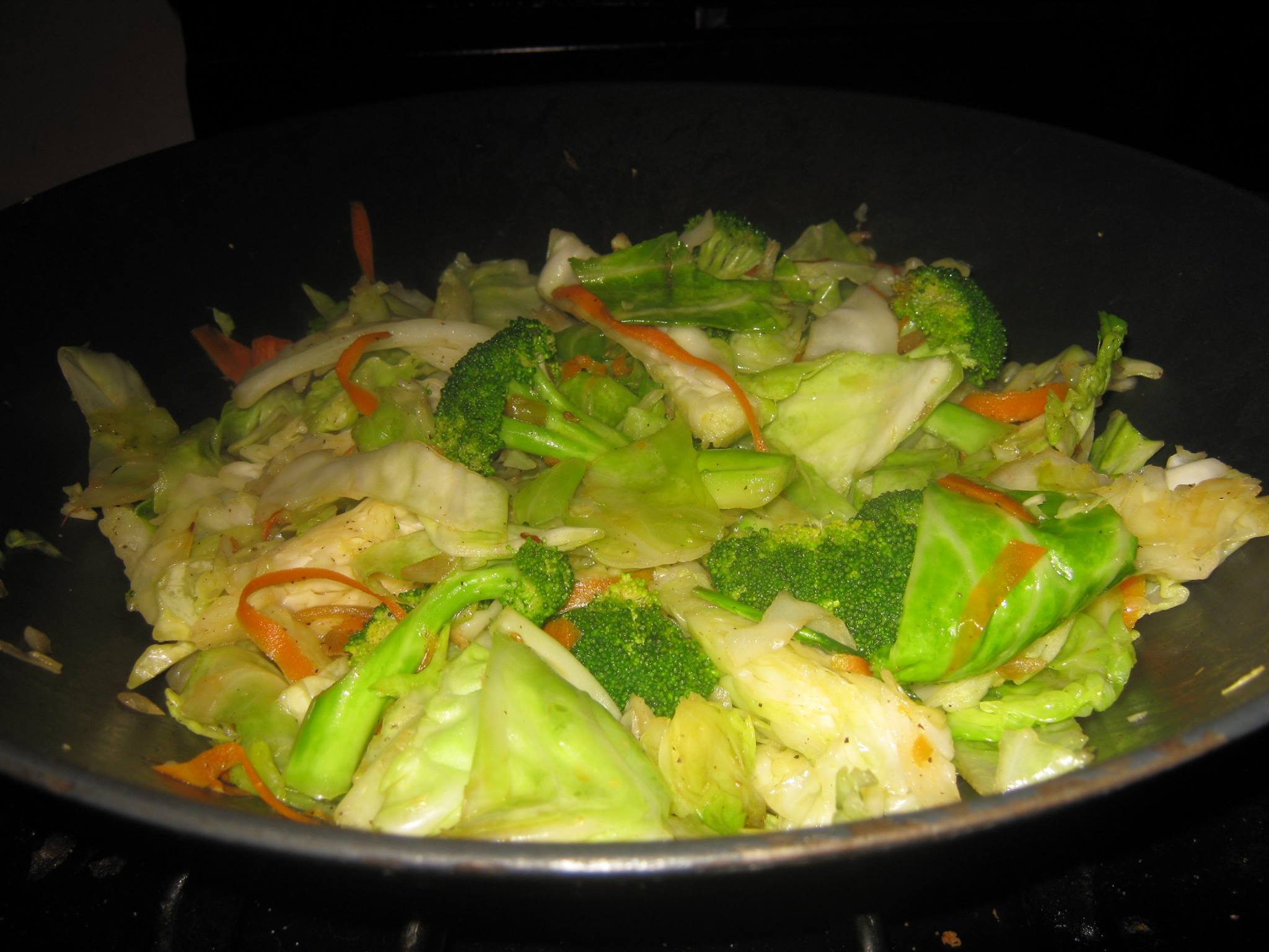Cooked green cabbage, carrots, broccoli and onions recipe in a wok