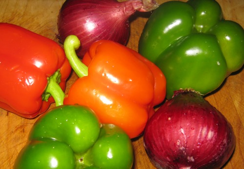 Whole bell peppers and red onions on a cutting board