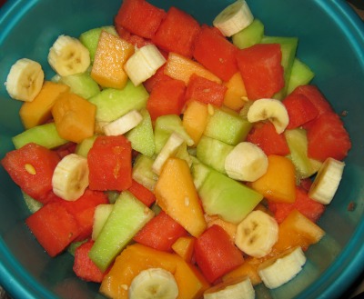 Fruit bowl containing watermelon, bananas, and orange and green cantaloupe